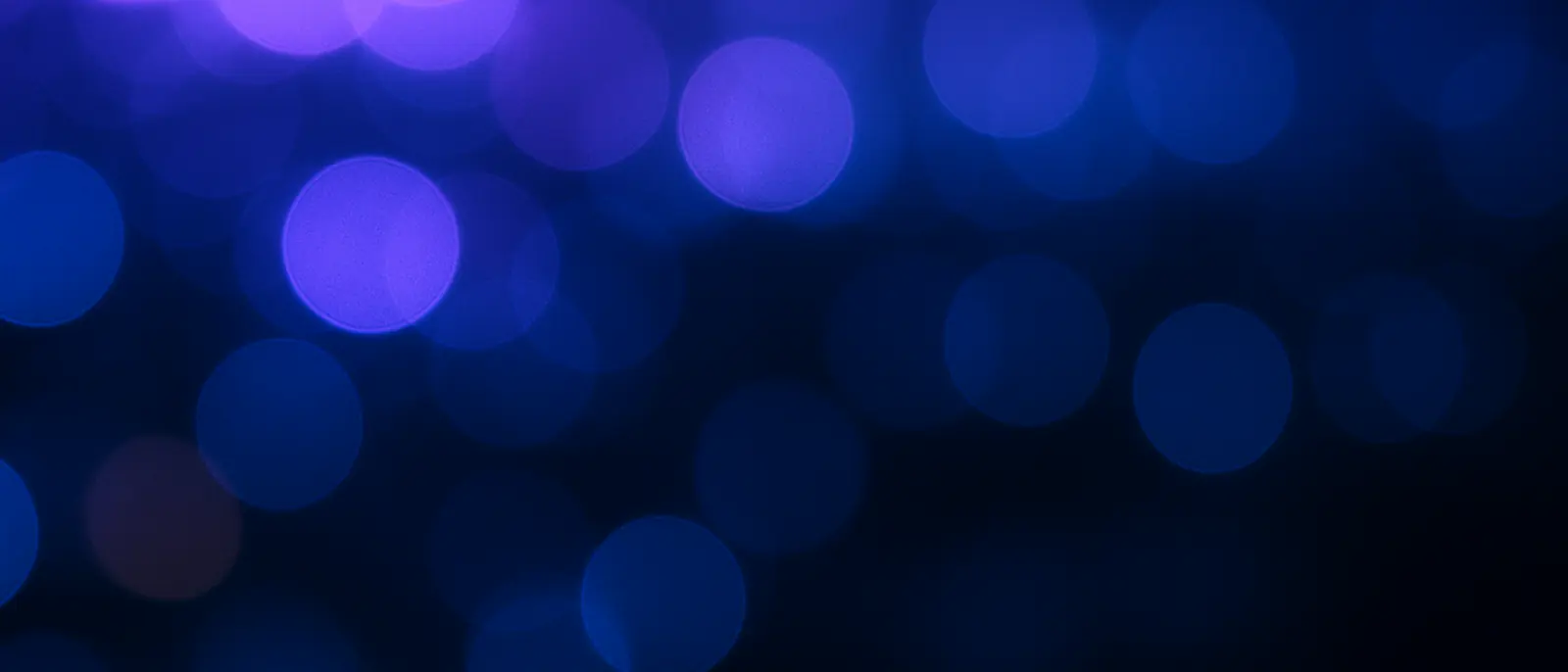 Luzes de cidade completamente desfocadas formando círculos suaves em tons de violeta e azul.